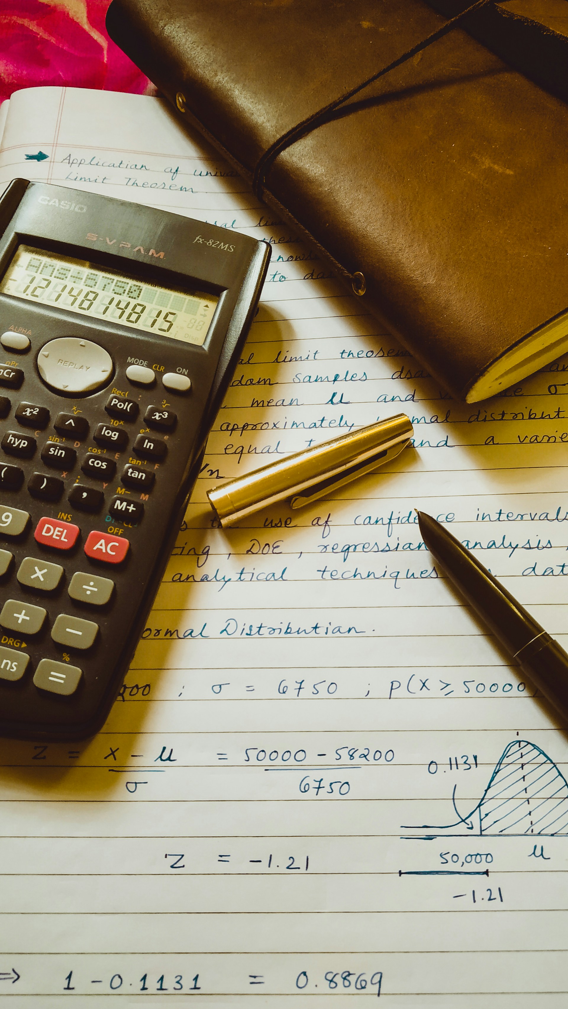 Une calculatrice scientifique, des notes techniques manuscrites avec des calculs statistiques, et un carnet en cuir sur un bureau
